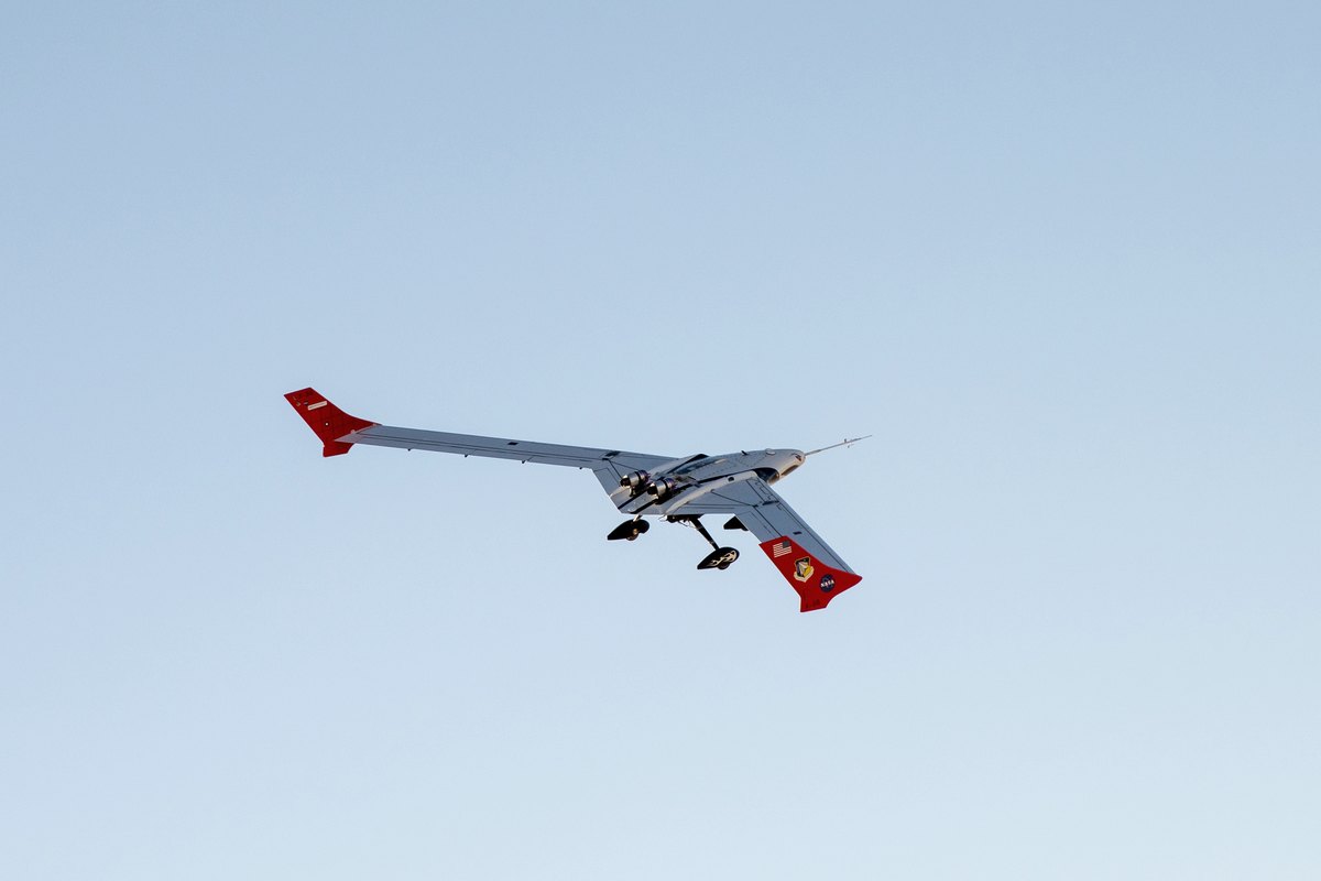 X-56A flexible-wing research aircraft banking in a pale blue sky, red fins at each wing tip