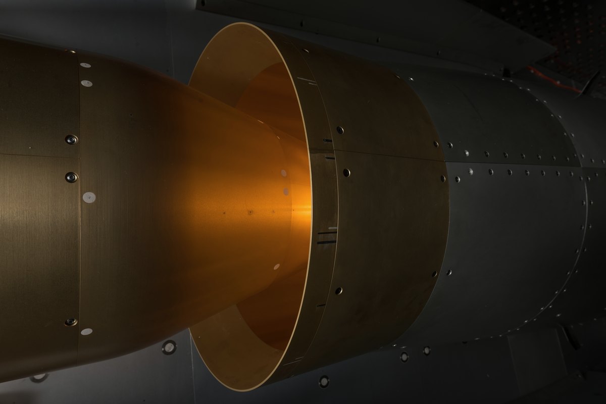 Close view of a gold-lit wind tunnel nozzle set in dark riveted metal panels